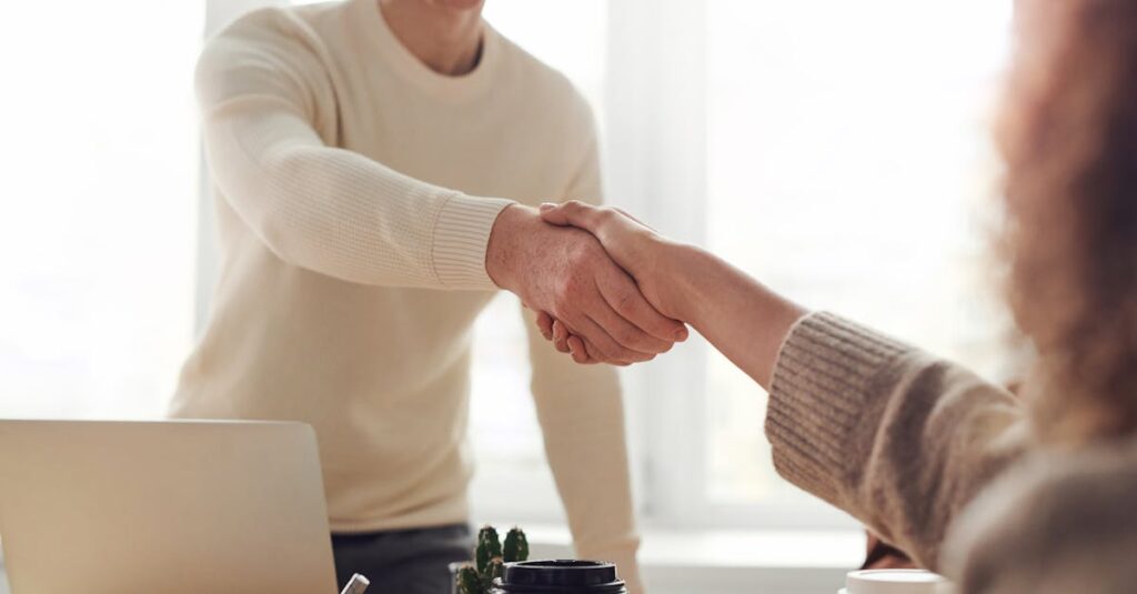 Close-up of professionals shaking hands over coffee in a modern office.